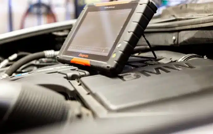 Diagnostic & Electrical Repair In Castle Rock CO At Titan Auto Tech European & Import Auto Repair. A diagnostic tablet device is connected to the engine of a BMW vehicle, displaying information on its screen while the car hood is open.