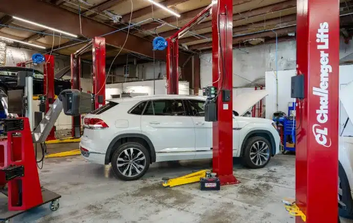 Preventative Maintenance In Castle Rock CO At Titan Auto Tech European & Import Auto Repair. A white SUV is parked inside an auto repair shop, surrounded by red vehicle lifts and various automotive equipment. The ceiling features exposed beams and hanging wires.