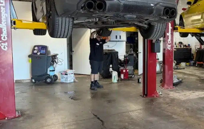Transmission Repair & Replacement In Castle Rock CO At Titan Auto Tech European & Import Auto Repair. A mechanic works under a black car lifted on a red hydraulic lift in an auto repair shop. Various tools and equipment are visible around the garage.