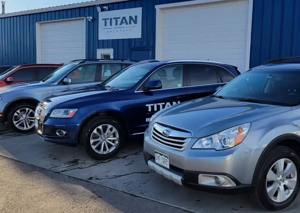 Vehicles We Service In Castle Rock CO At Titan Auto Tech European & Import Auto Repair. Three parked cars in front of a blue building with white garage doors and a sign reading TITAN AUTOTECH. The cars are different models, and one has TITAN branding on the side.