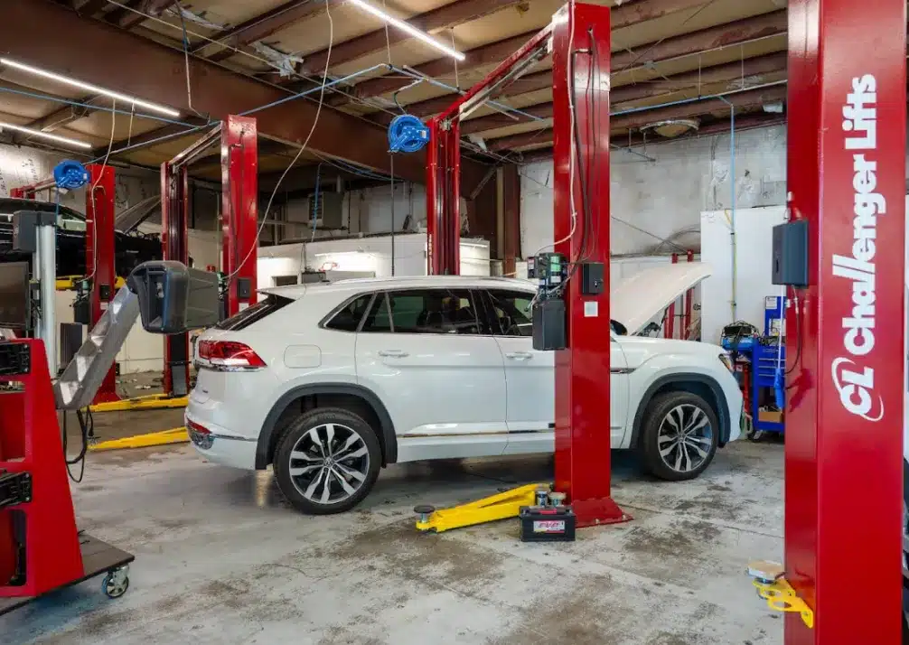 Preventative Maintenance In Castle Rock CO At Titan Auto Tech European & Import Auto Repair. A white SUV is parked inside an auto repair shop, positioned between red vehicle lifts. The car’s hood is open, and various tools and equipment are visible around the workshop.