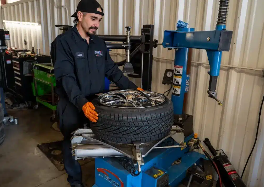 Tire Repair & Services In Castle Rock CO At Titan Auto Tech European & Import Auto Repair. A mechanic wearing an orange glove and dark uniform operates a tire changing machine, mounting a car tire onto a shiny rim inside an auto repair shop.