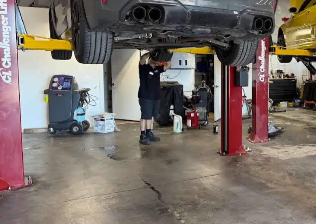 Transmission Repair In Castle Rock CO At Titan Auto Tech European & Import Auto Repair. A mechanic works under a raised car on a hydraulic lift inside a garage, with tools and equipment visible around the workspace.