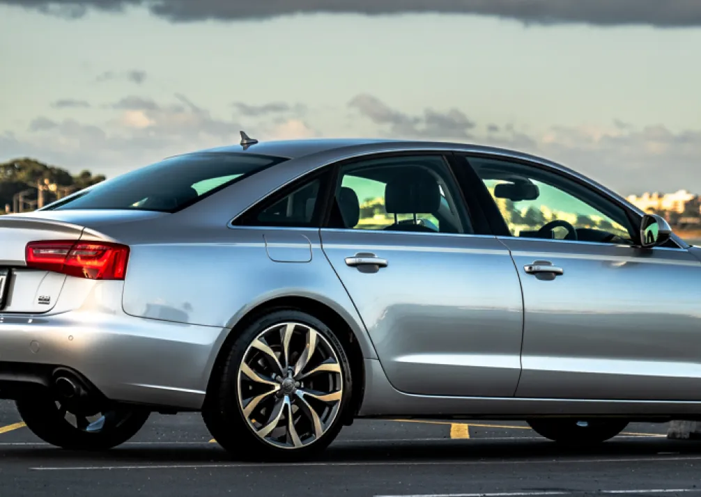 Audi Repair In Castle Rock CO At Titan Auto Tech European & Import Auto Repair. A silver sedan with black and silver alloy wheels is parked in an empty lot under a cloudy sky, viewed from the side and slightly behind.