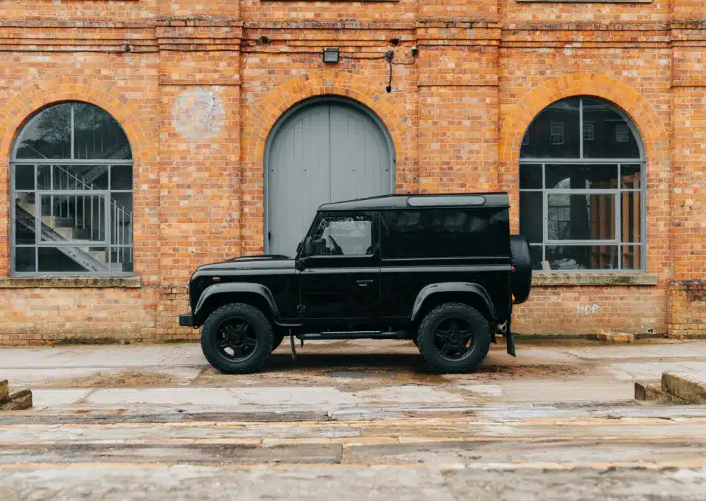 Land Rover Repair In Castle Rock CO At Titan Auto Tech European & Import Auto Repair. A black off-road vehicle is parked in front of a brick building with large arched windows and a gray arched door.