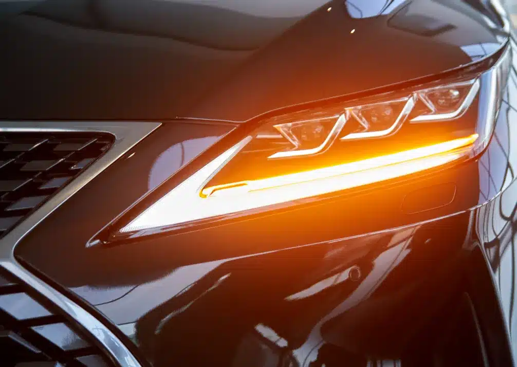 Lexus Repair In Castle Rock CO At Titan Auto Tech European & Import Auto Repair. Close-up of a cars front headlight with a sleek, modern design, showing the amber turn signal illuminated on a shiny black exterior. The image captures reflections on the smooth car surface.