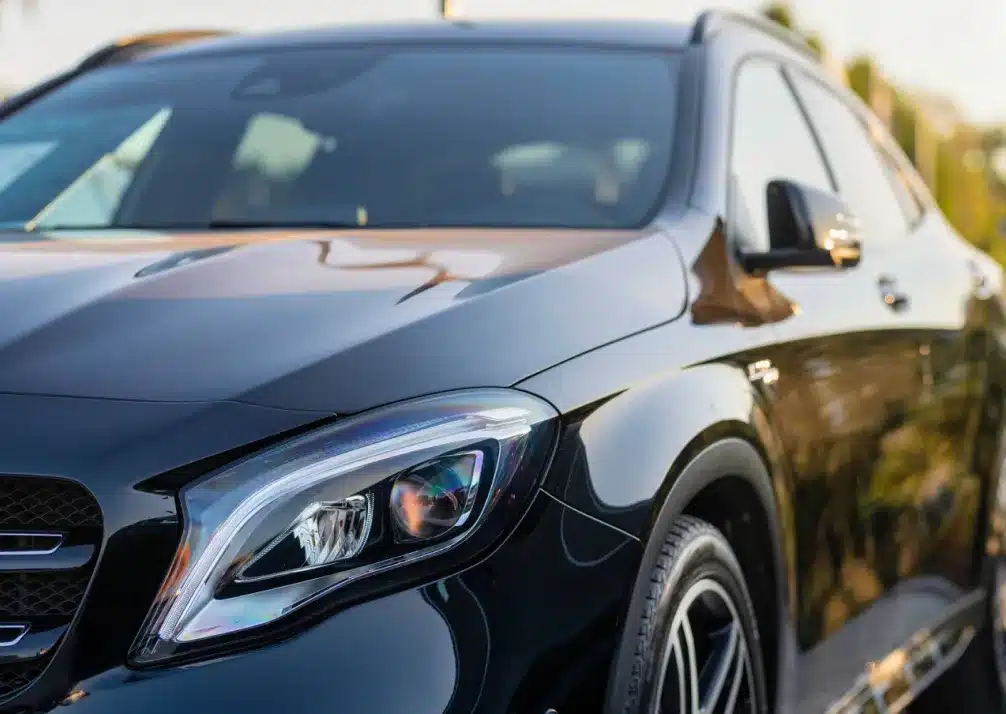 Mercedes Repair In Castle Rock CO At Titan Auto Tech European & Import Auto Repair. Close-up of the front left side of a shiny black car, showing the headlight, front wheel, and part of the grille, with reflections visible on the car’s surface.