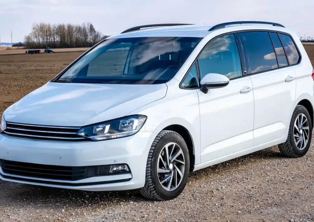 Volkswagen Repair In Castle Rock CO At Titan Auto Tech European & Import Auto Repair. A white minivan is parked on a gravel road next to a plowed field, with bare trees and a blue sky in the background.