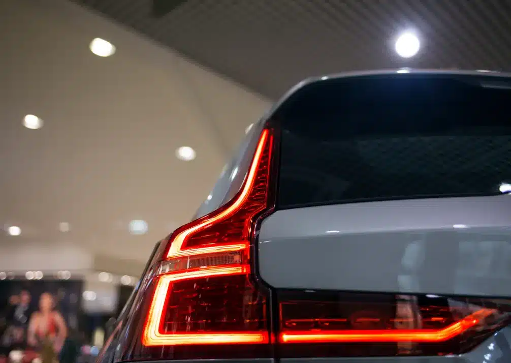 Volvo Repair In Castle Rock CO At Titan Auto Tech European & Import Auto Repair. Close-up of the rear LED taillight of a modern silver car, illuminated in a well-lit indoor setting with blurred background lights and people.