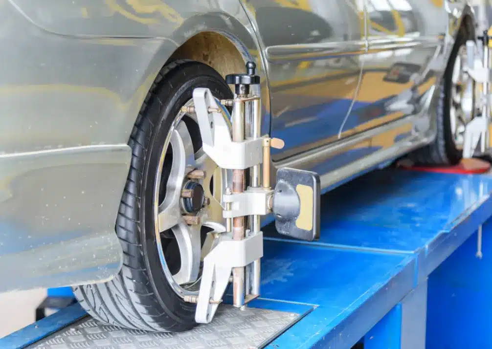 Wheel Alignment In Castle Rock CO At Titan Auto Tech European & Import Auto Repair. A car is on a blue platform in an auto shop, with a wheel alignment tool attached to the front tire, indicating that wheel alignment or maintenance is being performed.